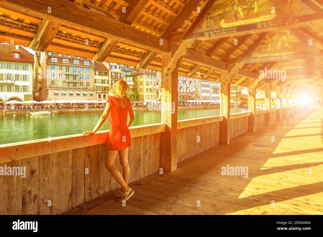 Blonde tourist woman at sunset sun rays in Lucerne city, under Chapel bridge on Reuss river. Historic covered wooden pedestrian bridge, famous Stock Photo