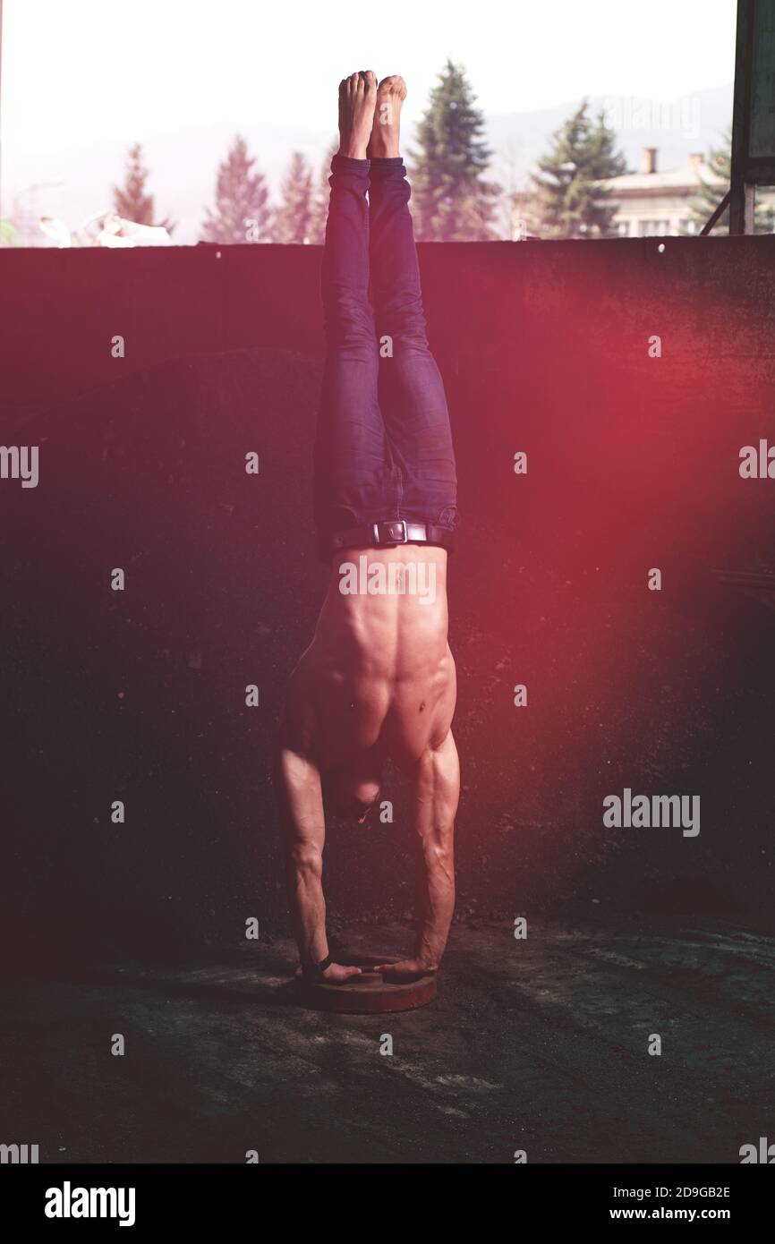 Young Man Keeping Balance on Hands in Warehouse - Muscular Athletic Bodybuilder Fitness Model Doing Handstand Push-up Stock Photo