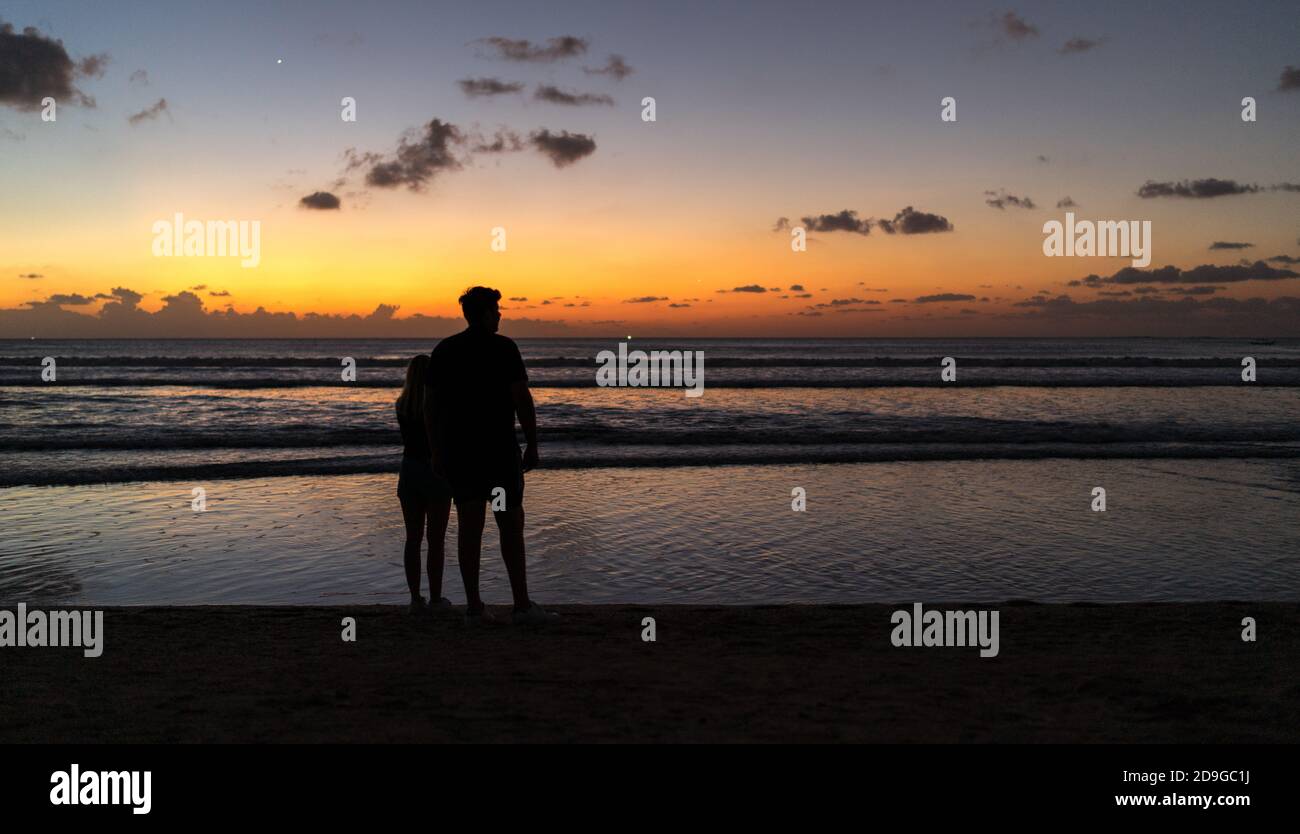 couple walking on the beach at sunset, A silhouette of a couple on the beach watching the golden sunset in Kuta, Bali Stock Photo