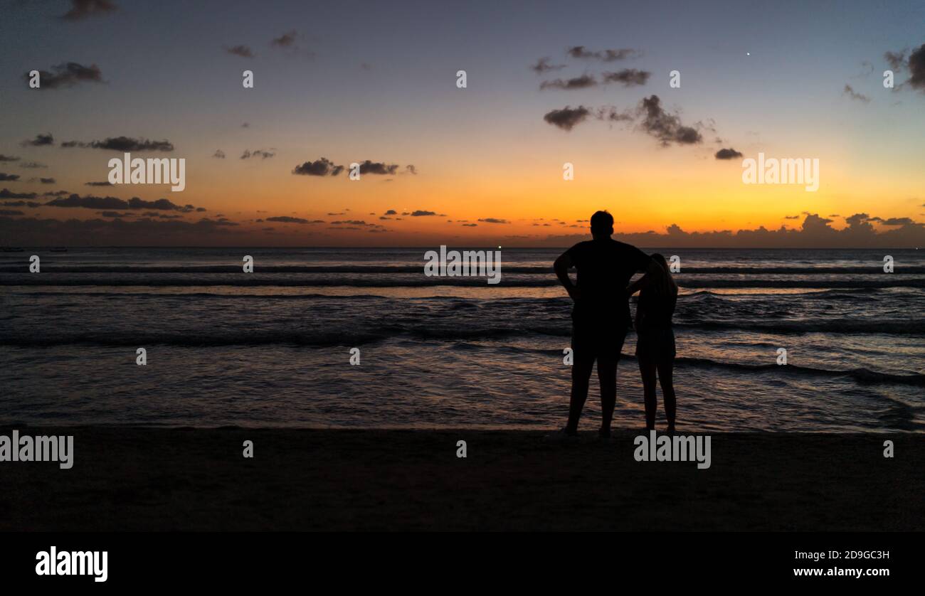 couple walking on the beach at sunset, A silhouette of a couple on the beach watching the golden sunset in Kuta, Bali Stock Photo