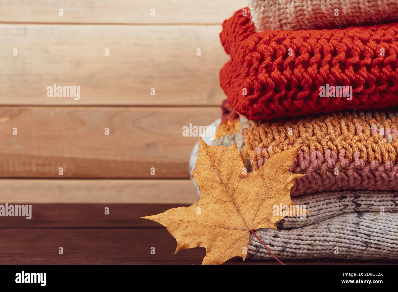 Stack of warm knitted sweaters. Autumn concept. Woolen jumpers and maple leaf on wooden background. Stock Photo