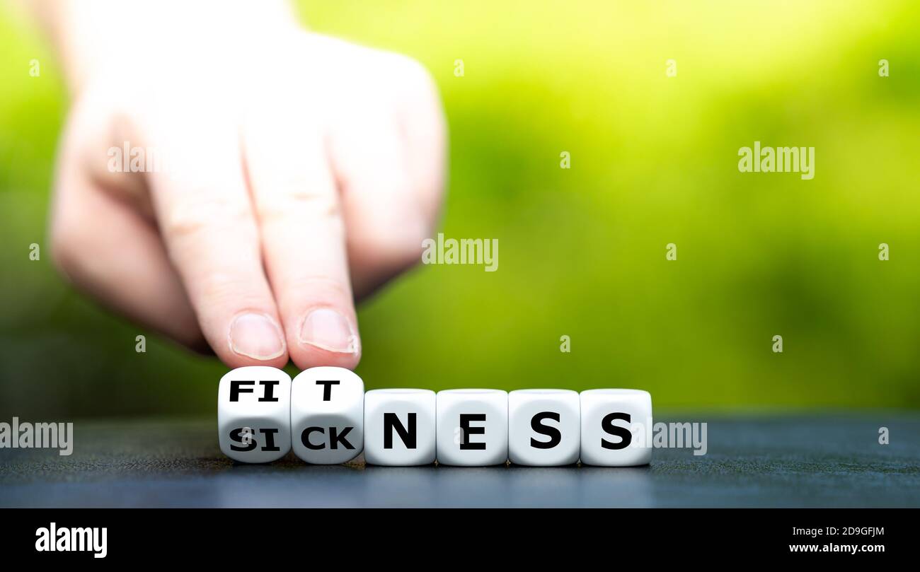 Hand turns dice and changes the word 'sickness' to 'fitness'. Stock Photo