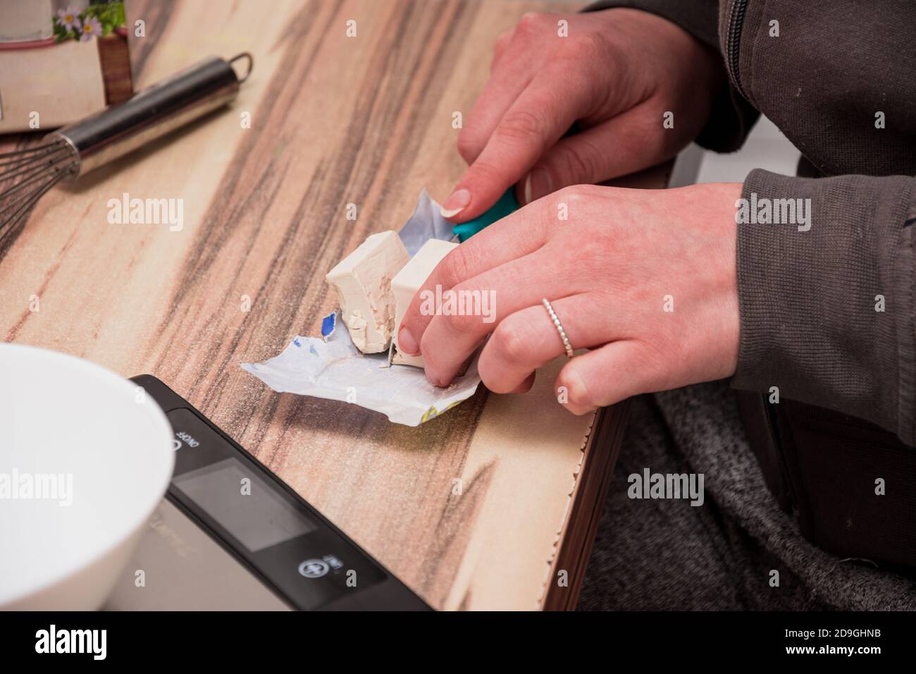 Cutting a cube of yeast on the packaging paper with a small knife Stock