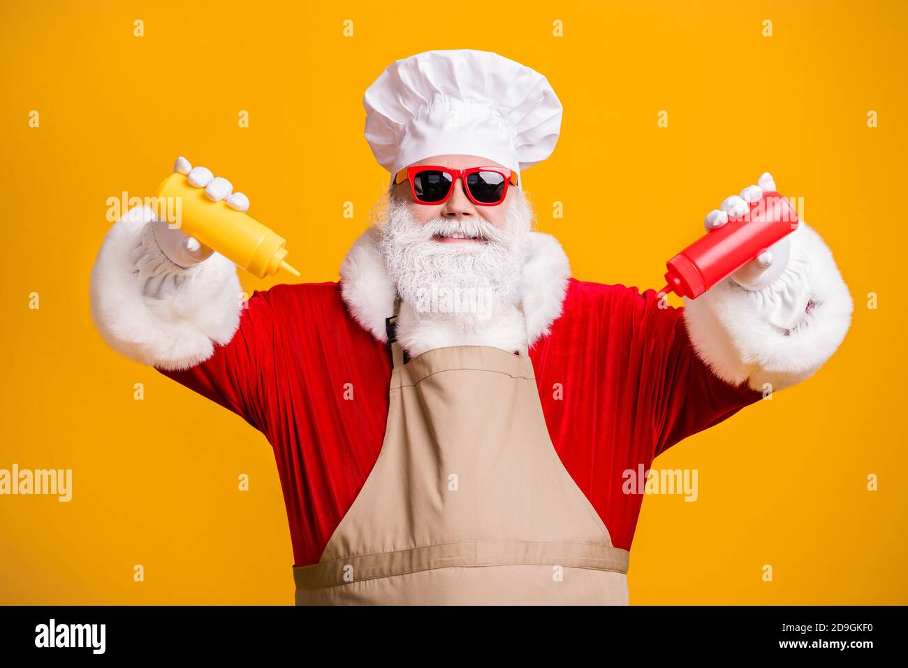 Photo of white grey hair beard santa claus in chef cap squeeze bottle ketchup mustard x-mas christmas eve feast wear apron sunglass isolated bright Stock Photo