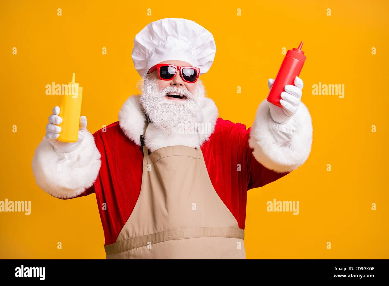 White grey beard hair santa claus in chef headwear cook x-mas christmas party snack hold mustard tomato sauce bottle wear sunglass apron isolated Stock Photo