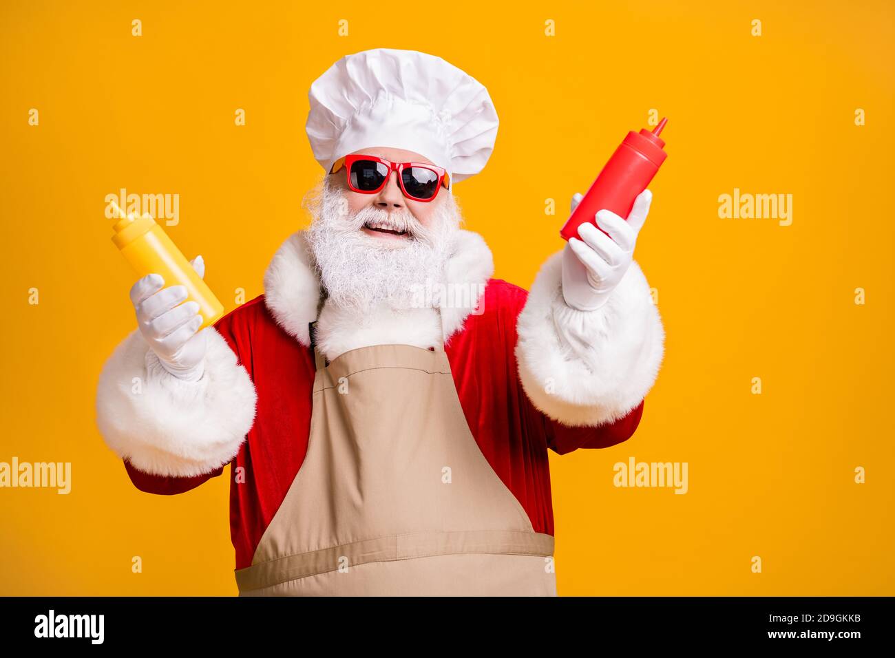 Funny santa claus in chef headwear cook x-mas christmas feast hold mustard tomato sauce bottle wear sunglass apron sunglass isolated bright shine Stock Photo