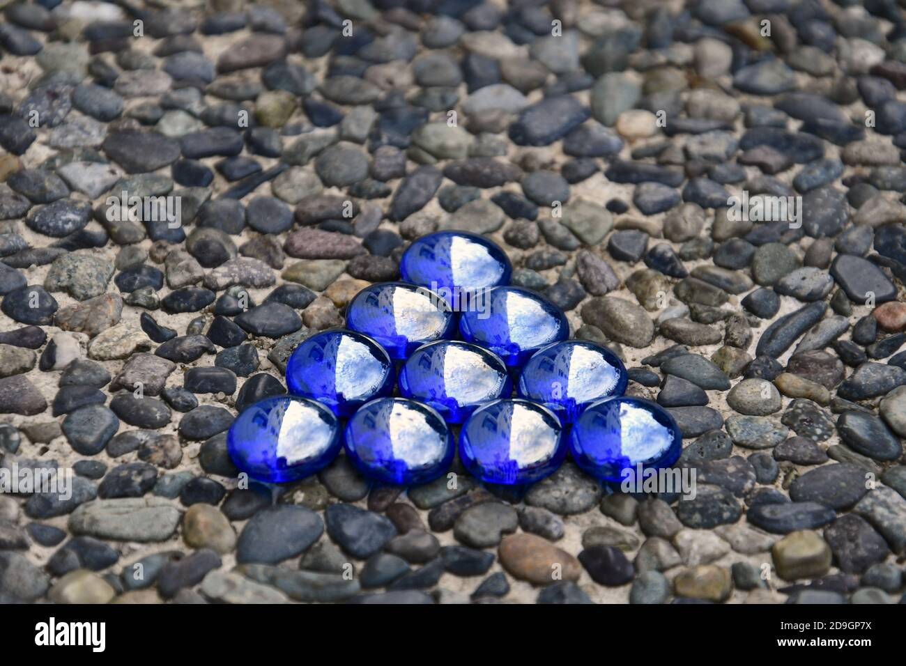Triangle of iridescent blue glass beads isolated on a pebbledashed stone background. Stock Photo