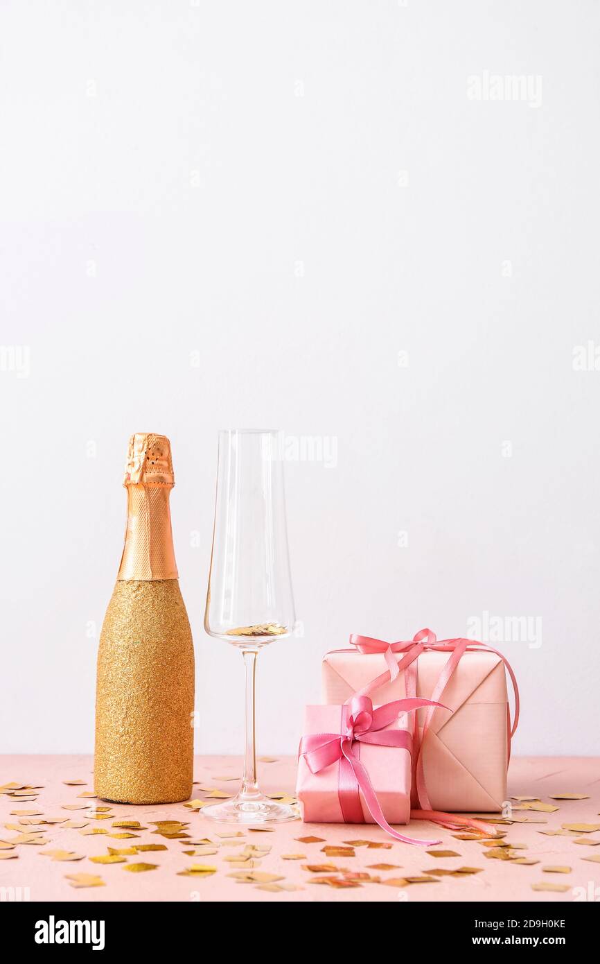 Bottle of champagne with glass and Christmas gifts on light background ...