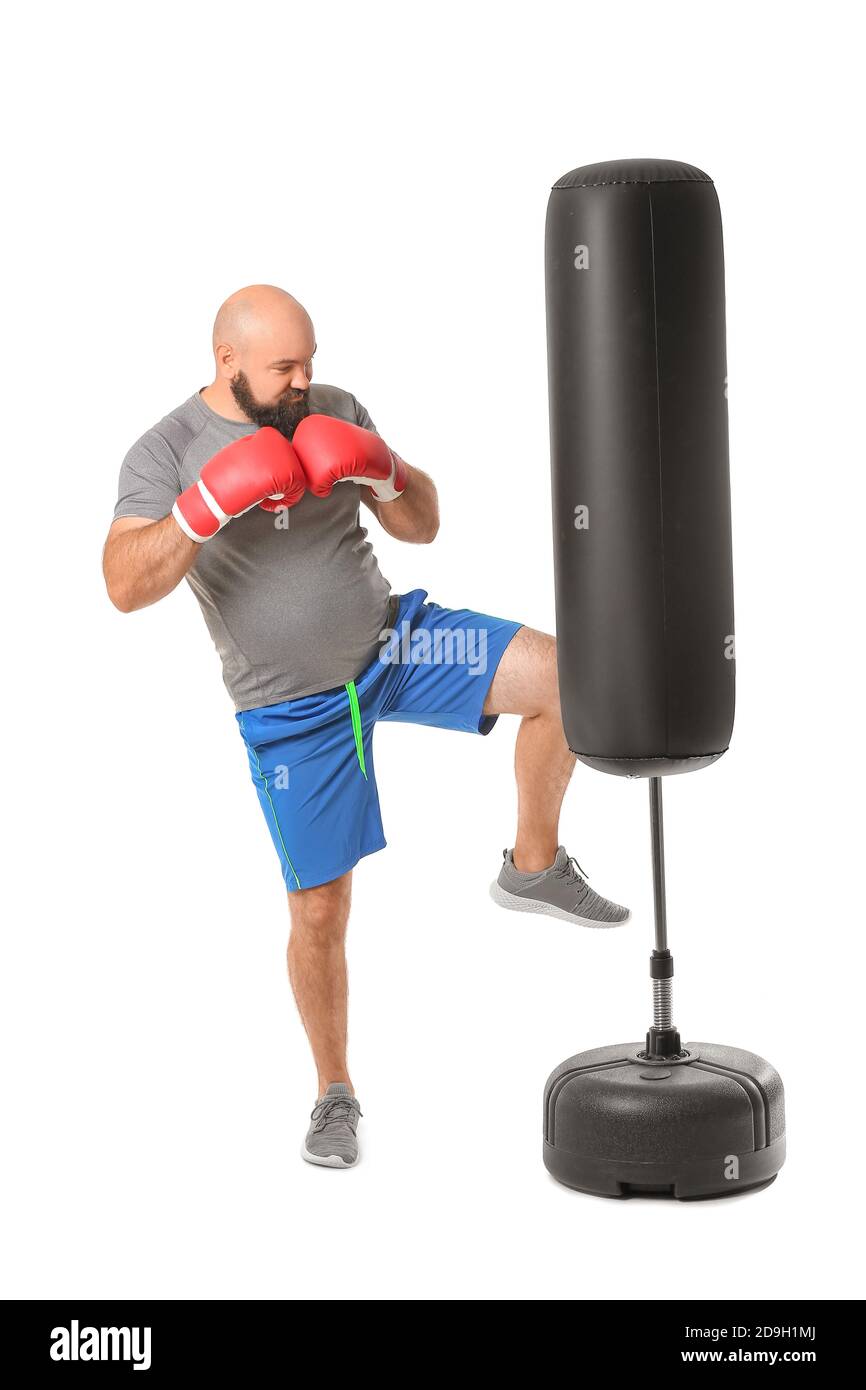 Overweight man in boxing gloves hitting punching bag on white
