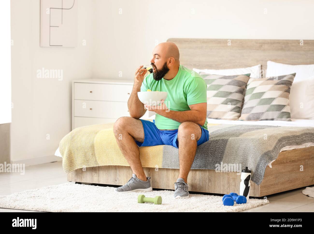Overweight man eating chips at home. Weight loss concept Stock Photo