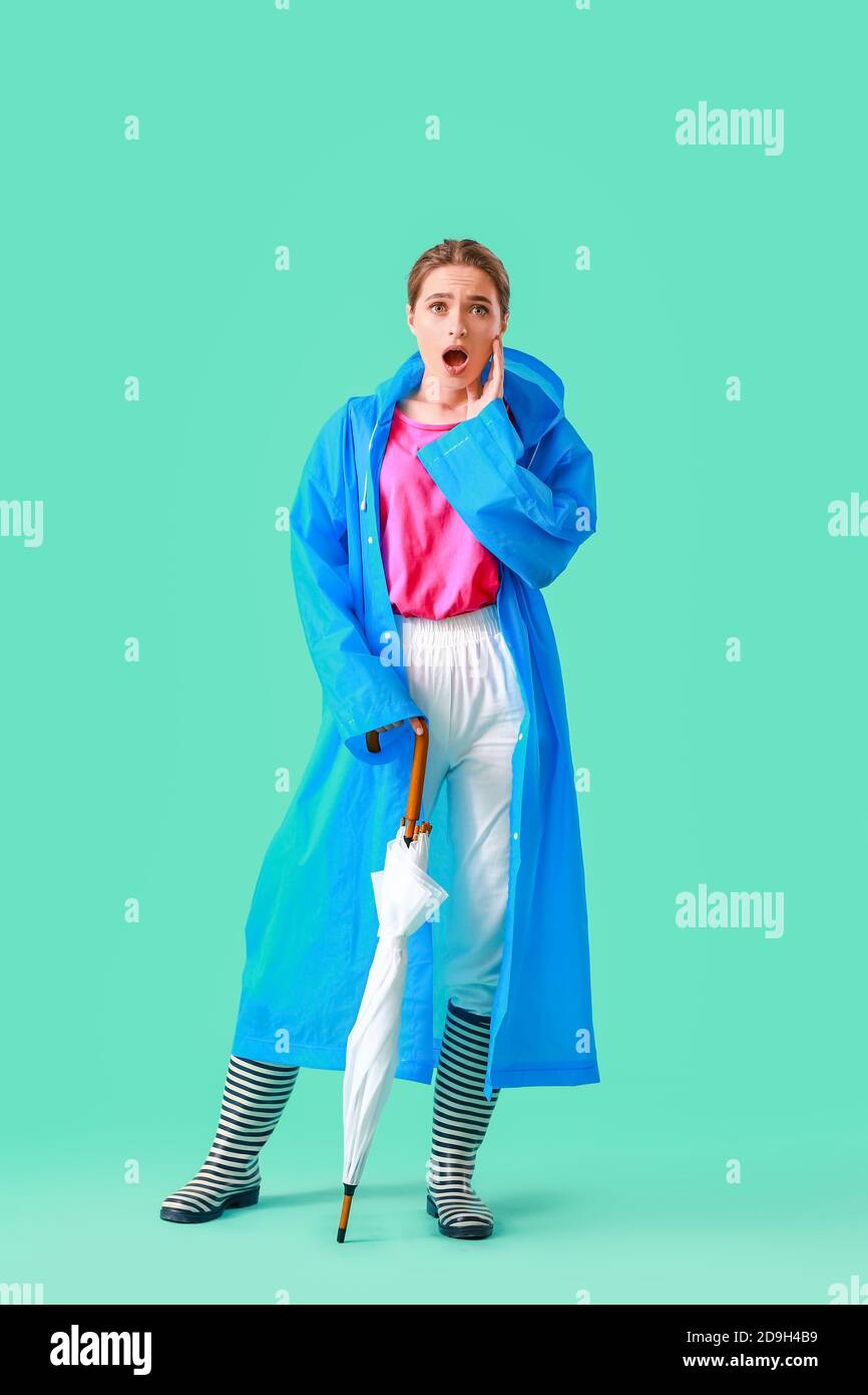 Beautiful young woman in raincoat and with umbrella on color background