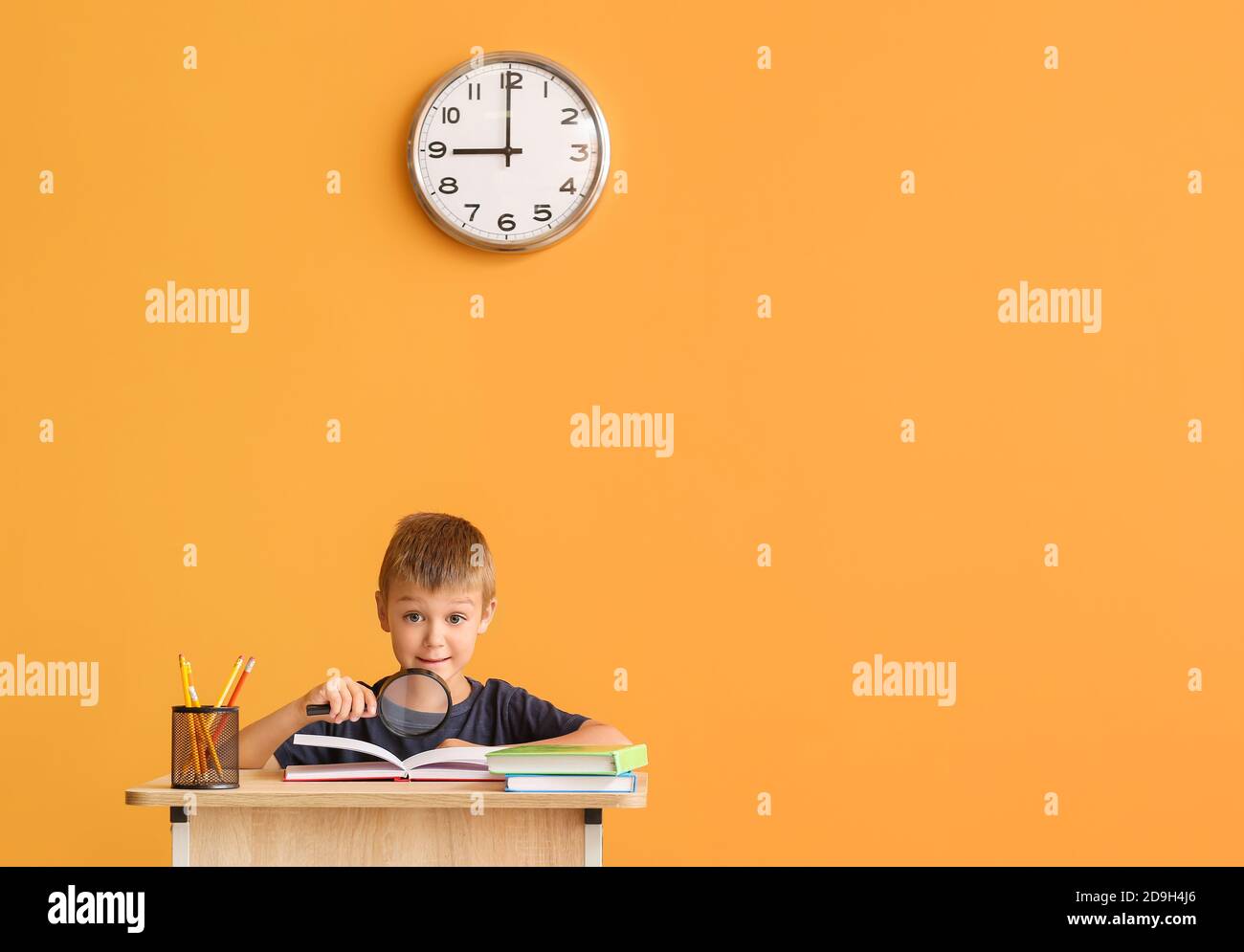 Cute pupil sitting at desk against color background Stock Photo - Alamy