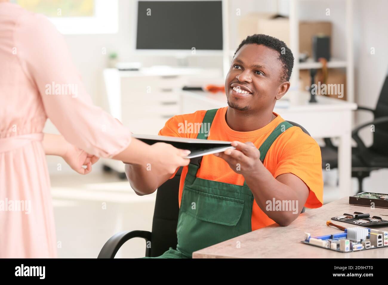African-American technician giving fixed laptop to owner in service center Stock Photo