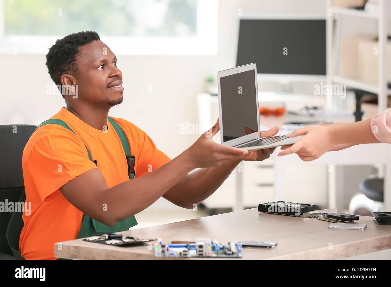 African-American technician giving fixed laptop to owner in service center Stock Photo
