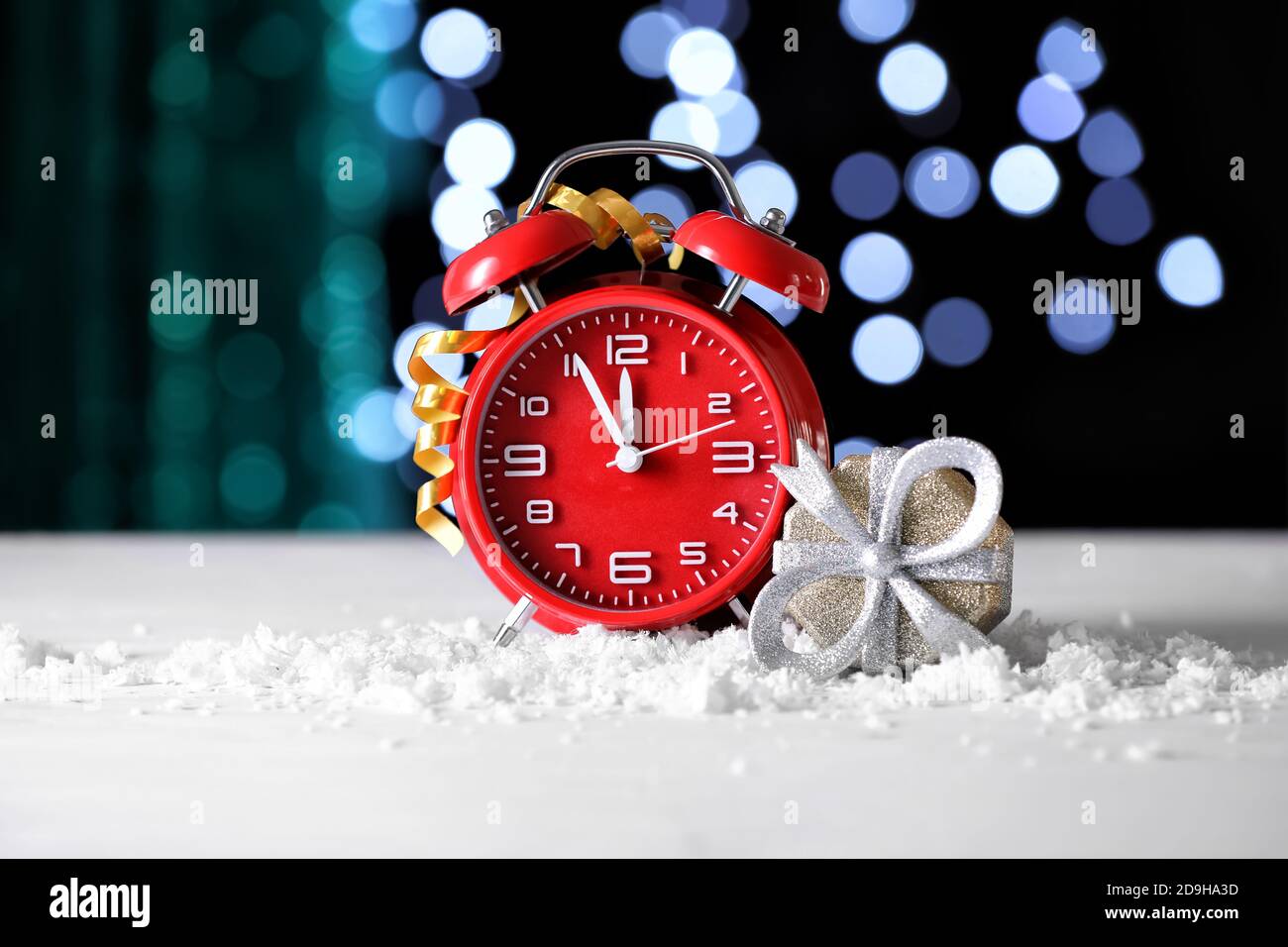 Christmas gift and alarm clock on table against blurred lights Stock Photo