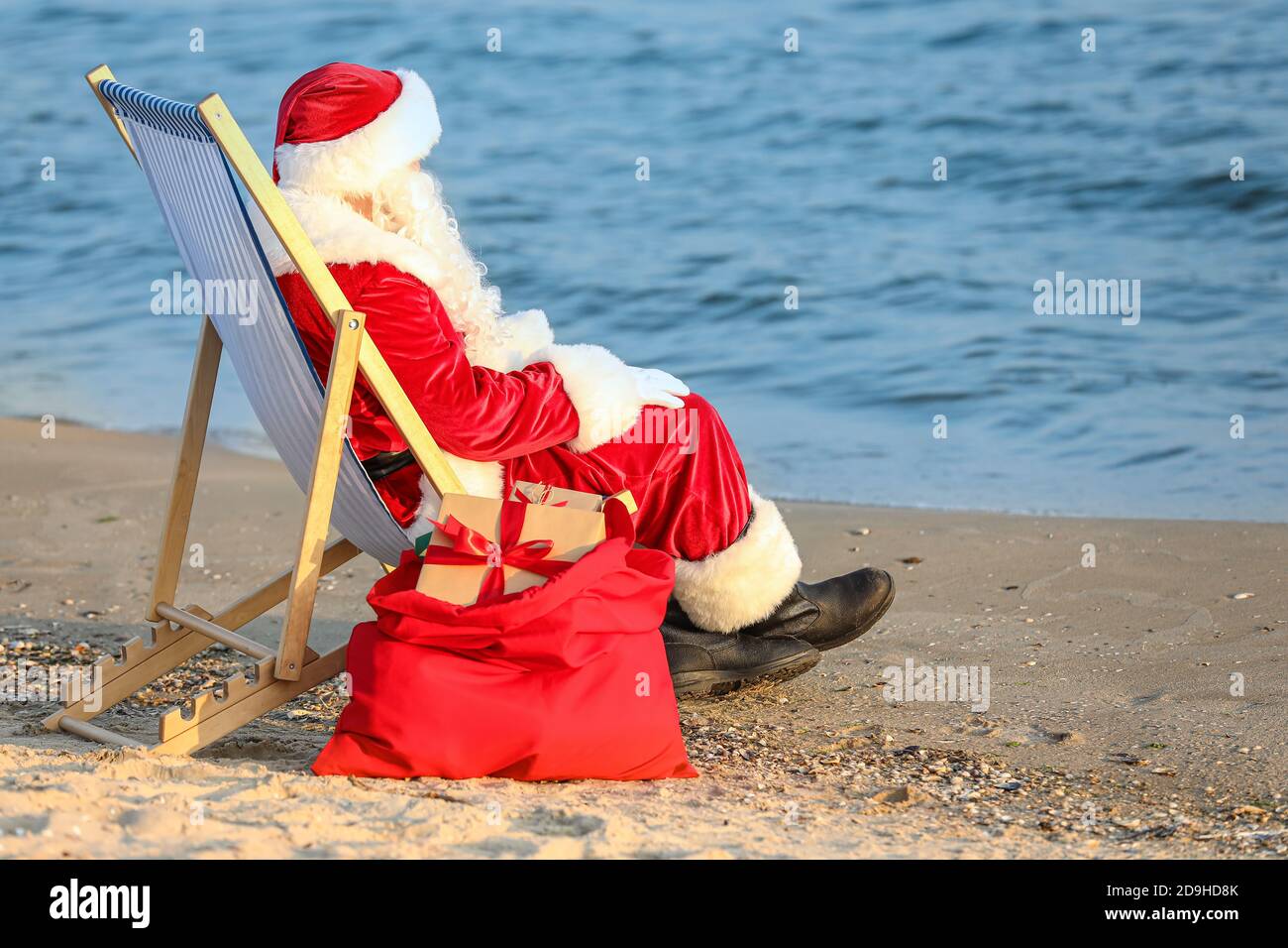 Santa Claus with Christmas gifts in bag resting on beach Stock Photo ...