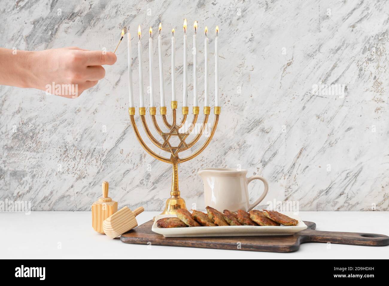 Woman lighting candles on menorah for Hanukkah on table with dreidels
