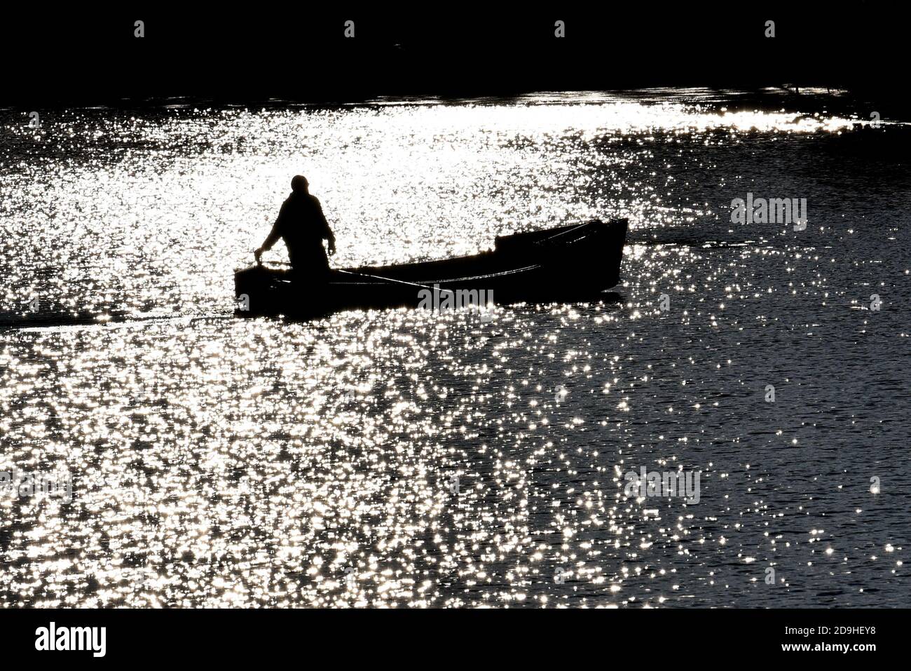 Fisherman is silhouetted as he heads out to dredge for seed mussels on the Midgell River on Prince Edward Island, Canada. Stock Photo