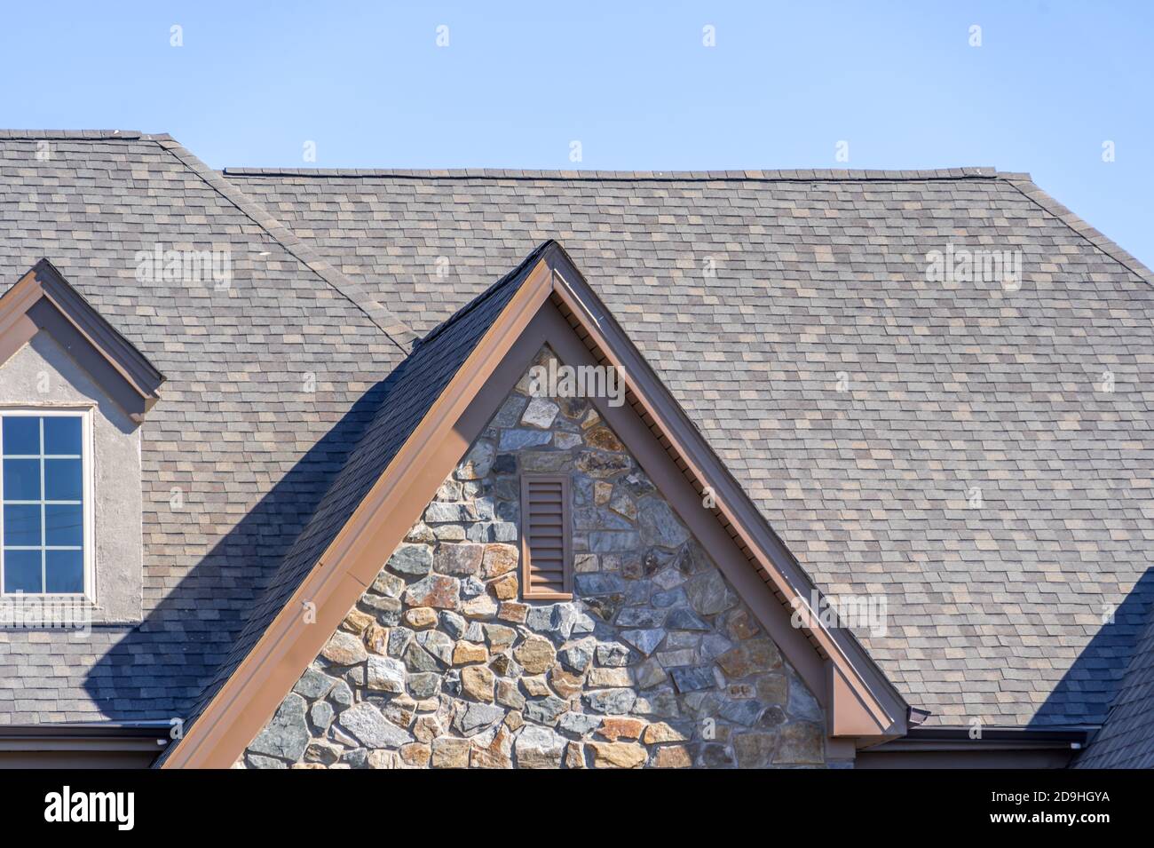 Double gable with dark stone veneer siding, with triangle shape peaks, on a pitched roof attic at an American single family home neighborhood USA, dou Stock Photo