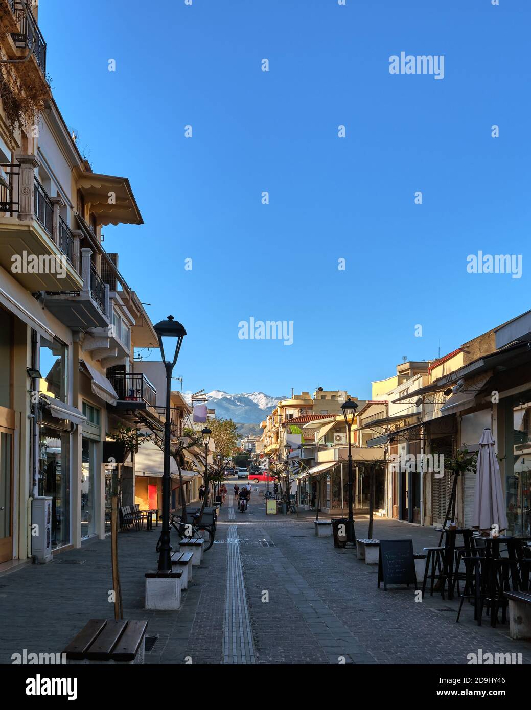 Typical street of Chania, Crete, Greece with shops, cafes and restaurants for evening promenade. No tourists, early morning. Snow on Cretan mountains Stock Photo