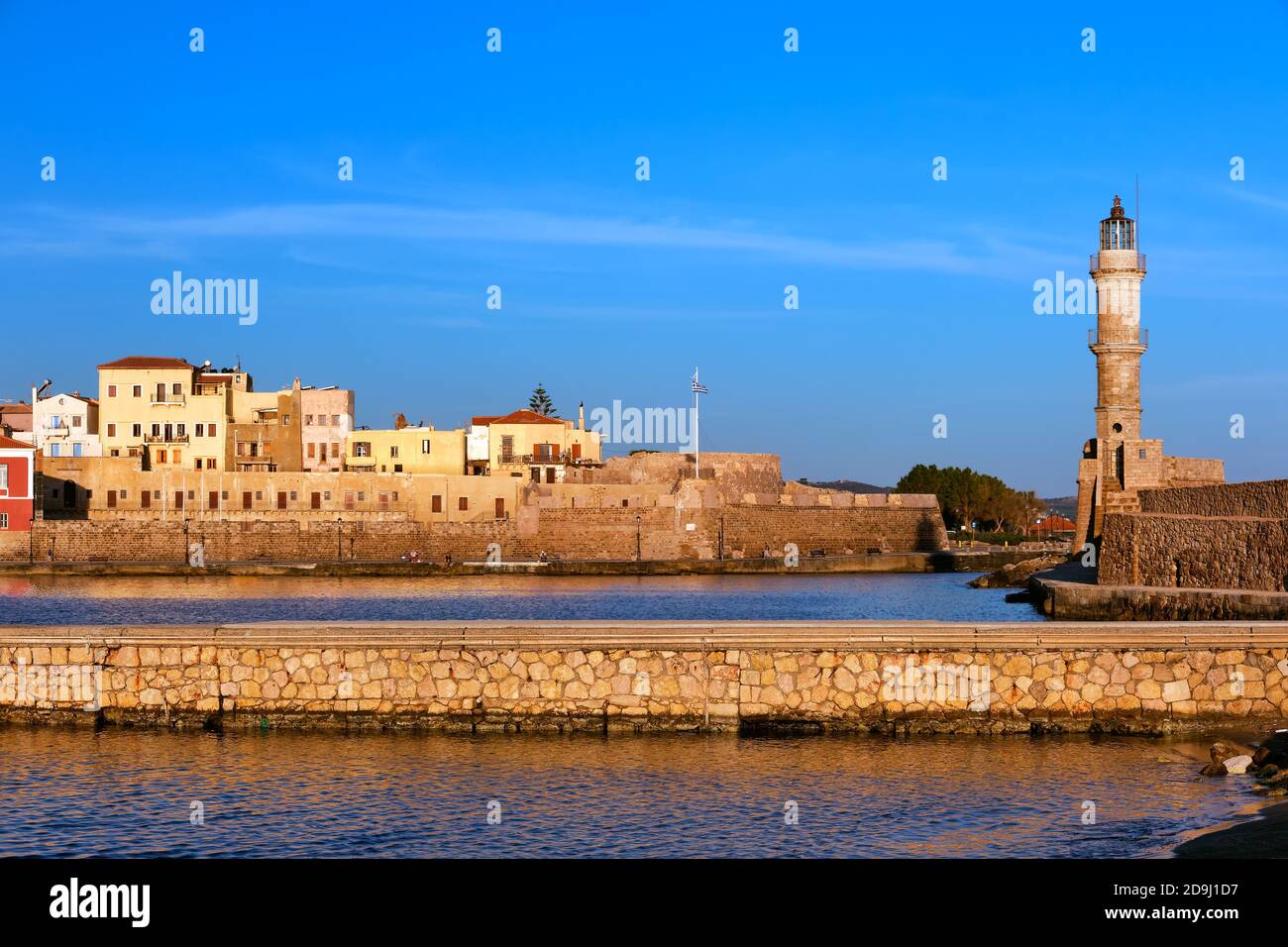 Beautiful morning view of Venetian Lighthouse, Firka castle walls and piers of Old Venetian harbour of Chania, Crete, Greece at golden hour.  Stock Photo