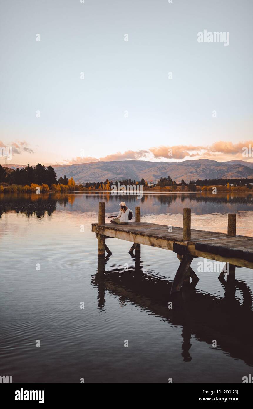 Vertical shot of a female sitting on the pier playing the guitar in Cromwell, New Zealand Stock Photo