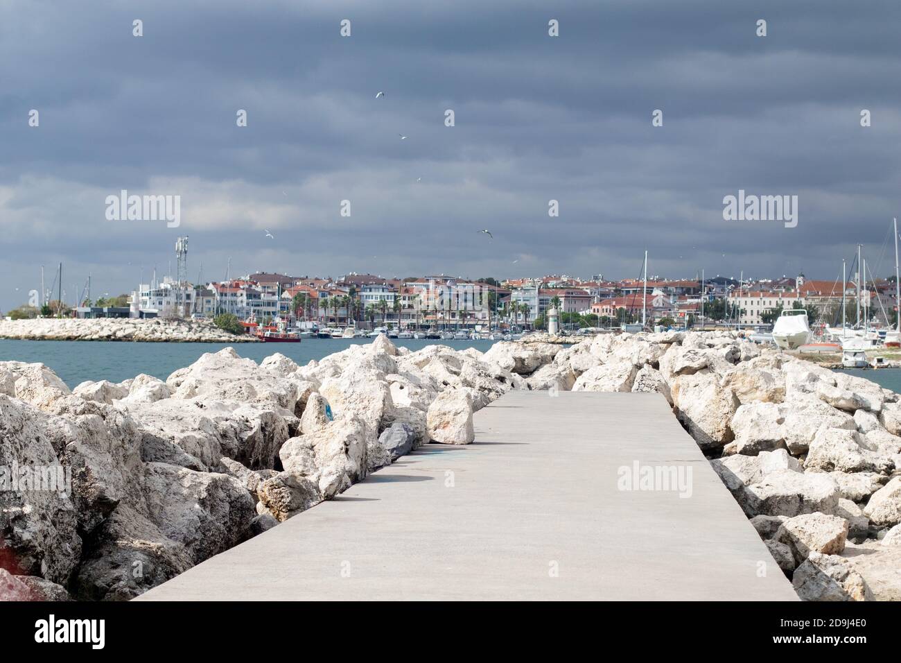 Rock embankment in the sea and pier parking for ships. Thunderous sky and seagulls Stock Photo