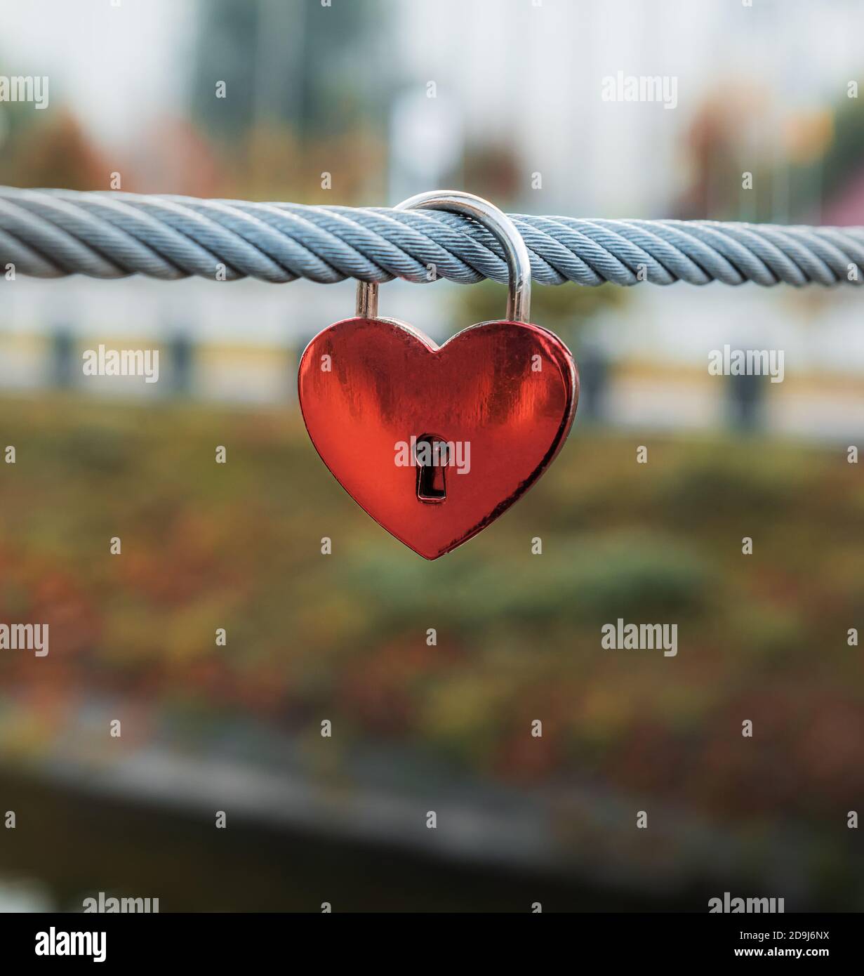 Red heart padlock on steel cable of bridge fence in Kharkov city in Ukraine. Unfocused cityscape in autumn colors at background. Selective focus. Copy Stock Photo