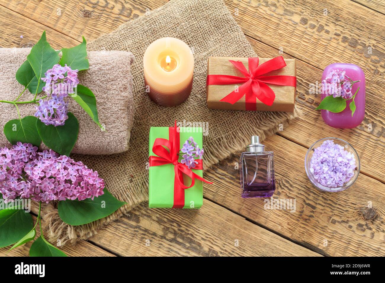 Terry towel, soap and sea salt for bathroom procedures, a burning candle, gift boxes, a bottle of perfume and lilac flowers on sackcloth and old woode Stock Photo