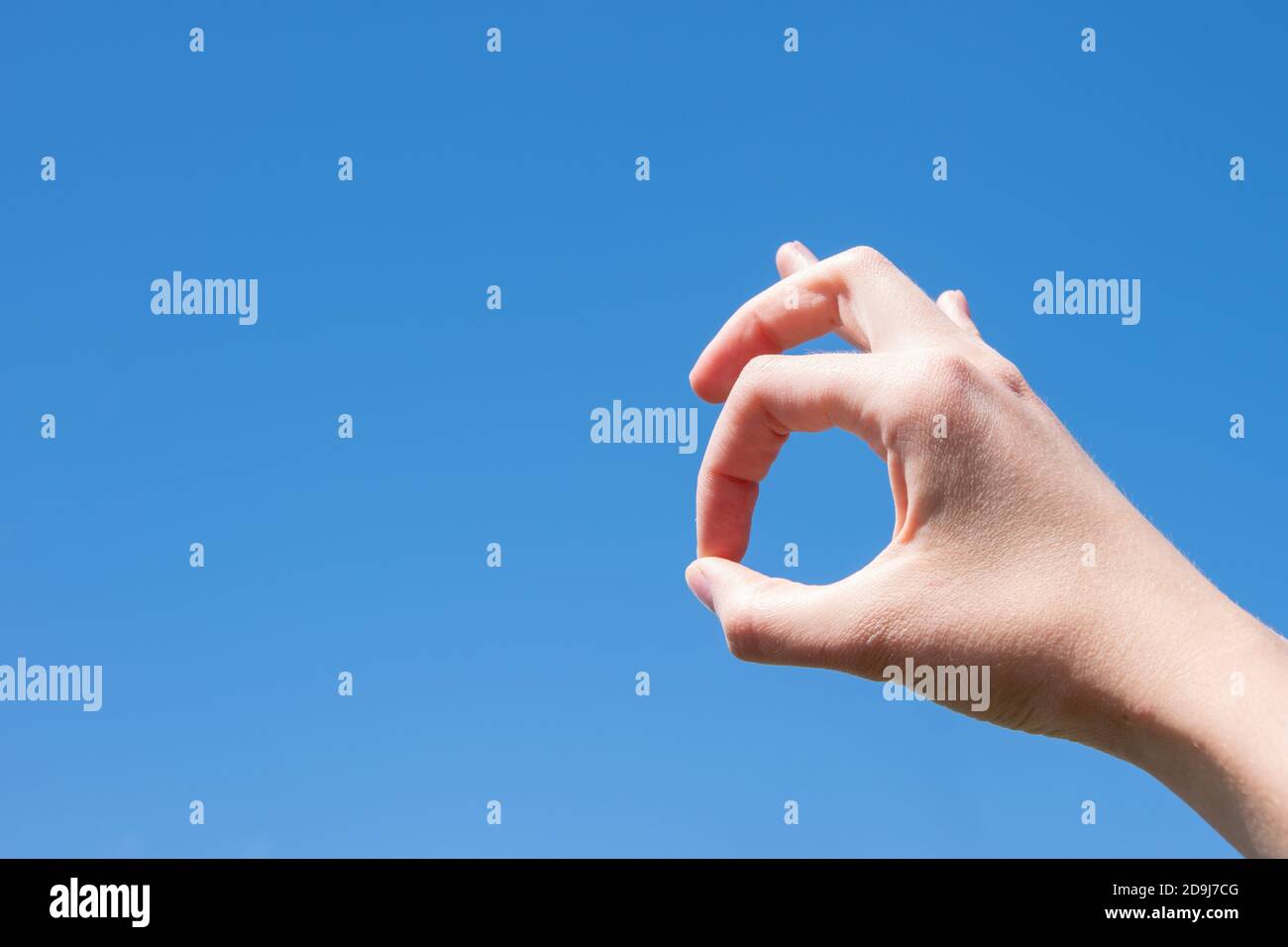 Closeup gesture of a woman hand making ok isolated against a blue sky background. Stock Photo