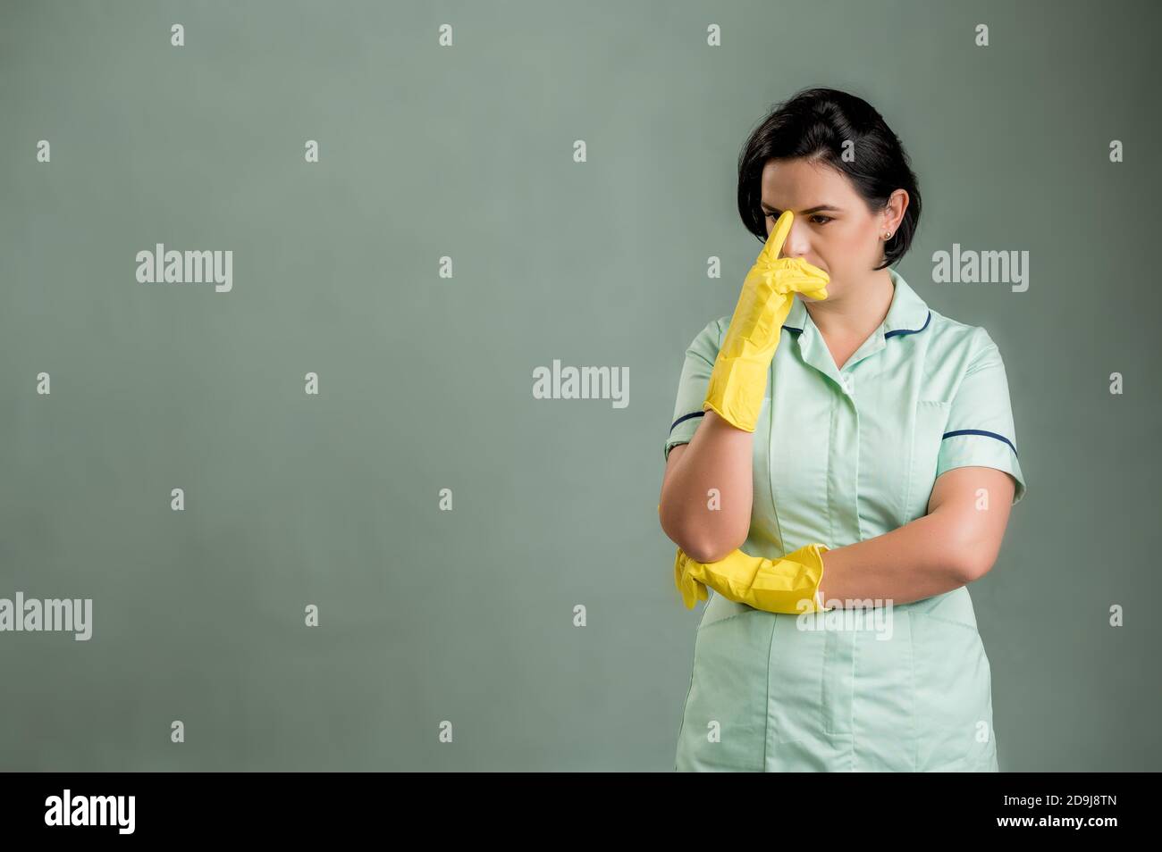 Young cleaning woman wearing a green shirt and yellow gloves, wondering ...