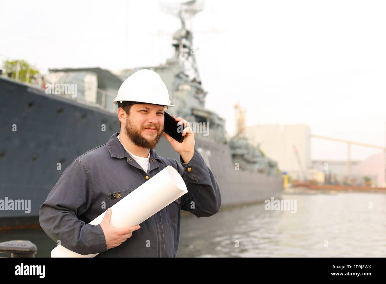 Marine engineer talking by VHF walkie talkie, holding papers near vessel in background. Stock Photo