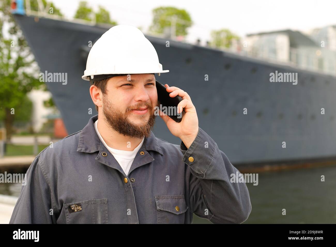 Marine first mate talking by VHF walkie talkie near vessel in background. Stock Photo