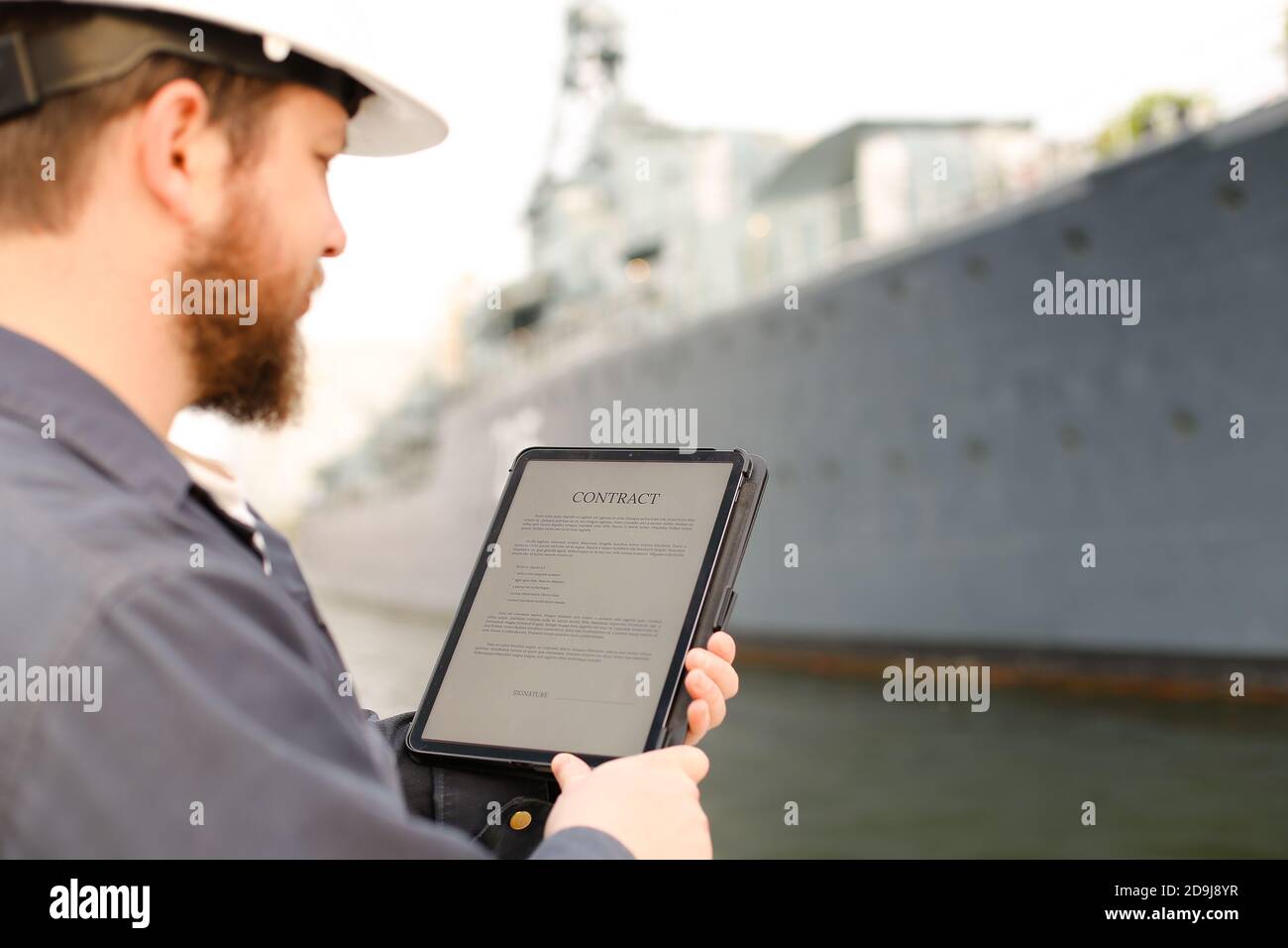 First mate reading contract on tablet near vessel in background. Stock Photo
