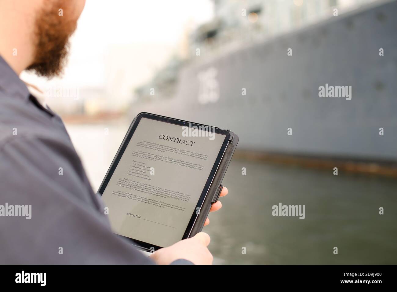 Marine engineer reading contract on tablet near vessel in background. Stock Photo