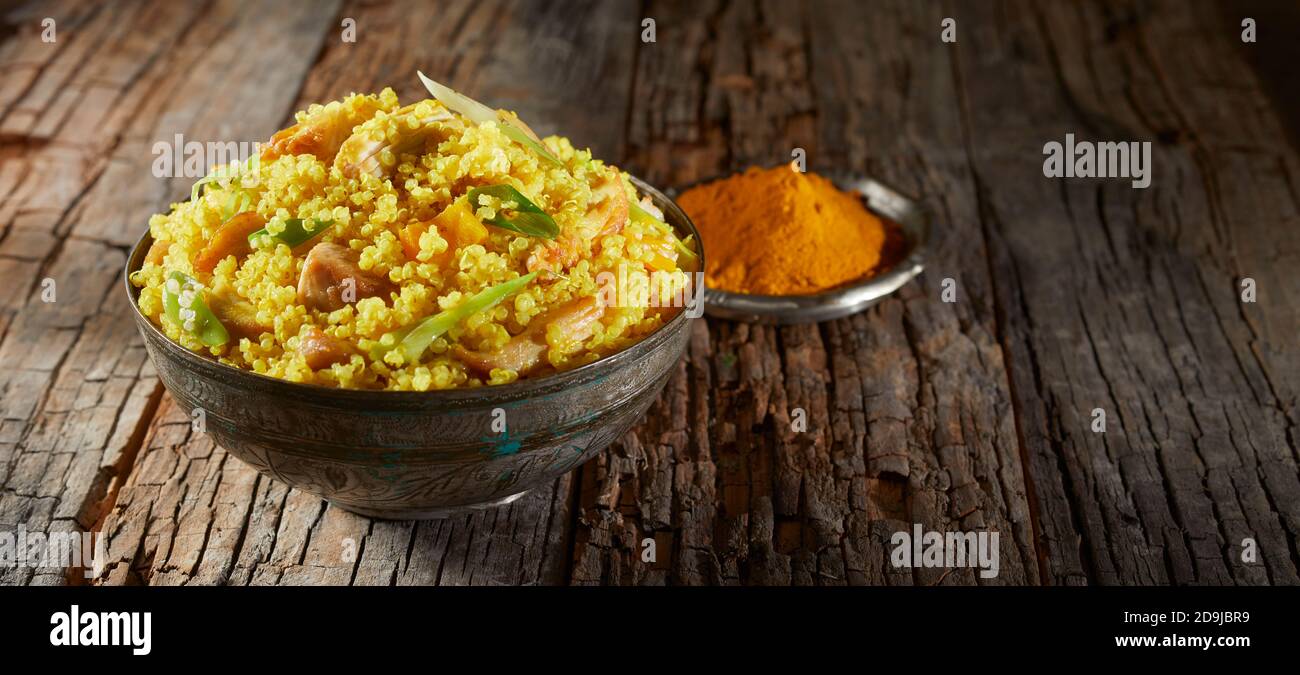 Heaped bowl of savory quinoa and couscous spiced with turmeric or saffron on a rustic wooden table in a panorama banner Stock Photo