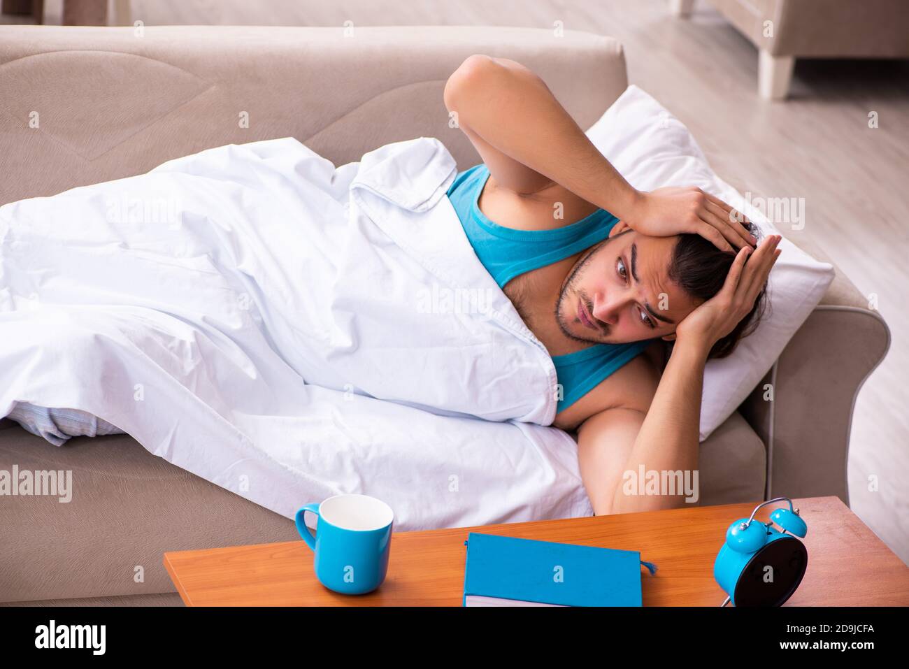 Young man lying on sofa in time management concept Stock Photo - Alamy