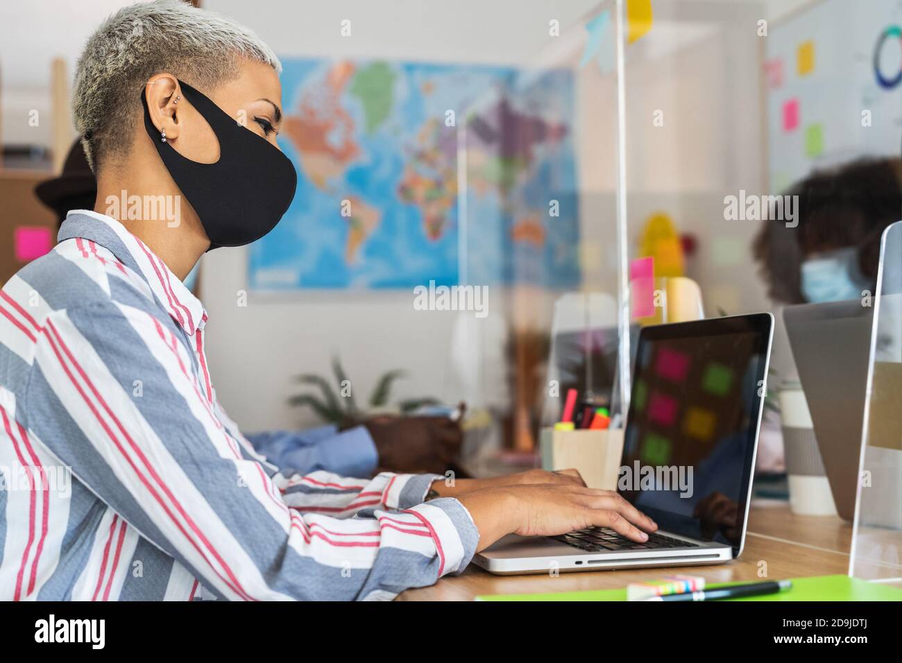 Young people in co-working creative space wearing surgical mask and keeping social distance to avoid corona virus spread Stock Photo