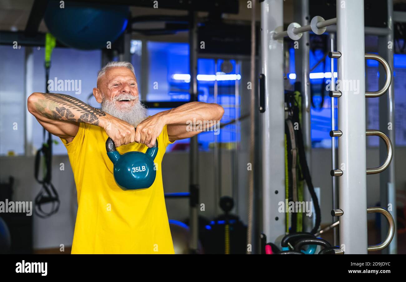 Senior fit man doing kettle bell exercises inside gym - Fit mature male