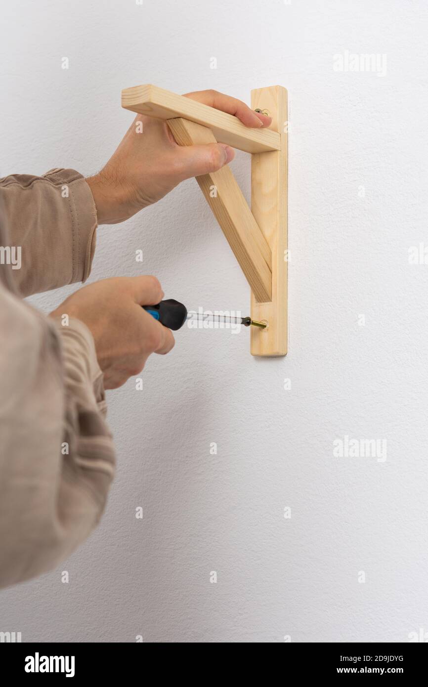 A man hangs a shelf in an apartment on a white wall, a worker fixes