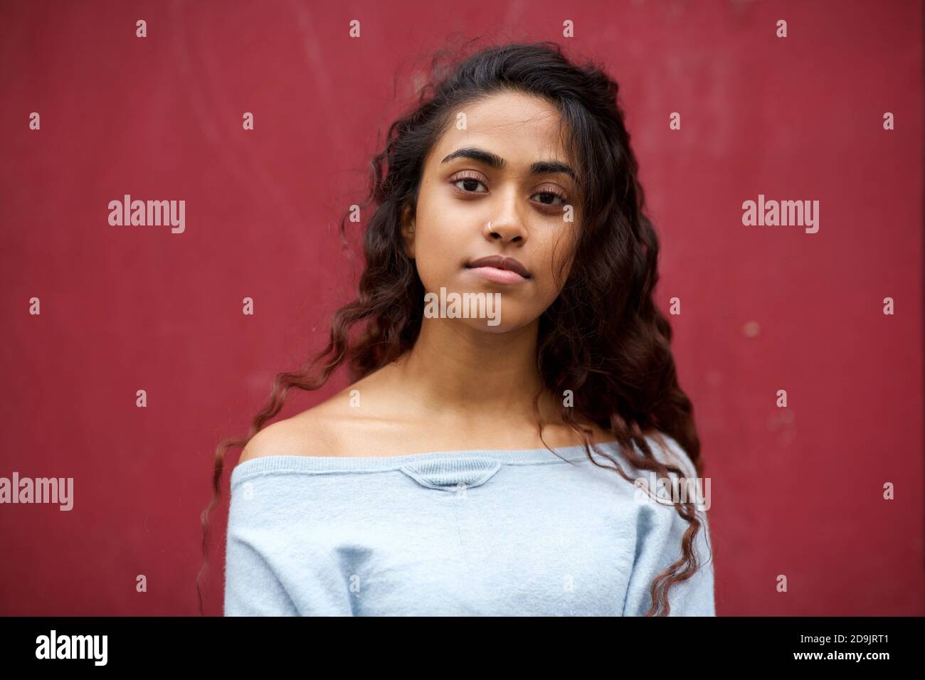 Close up portrait beautiful young Indian woman with long hair against red background Stock Photo