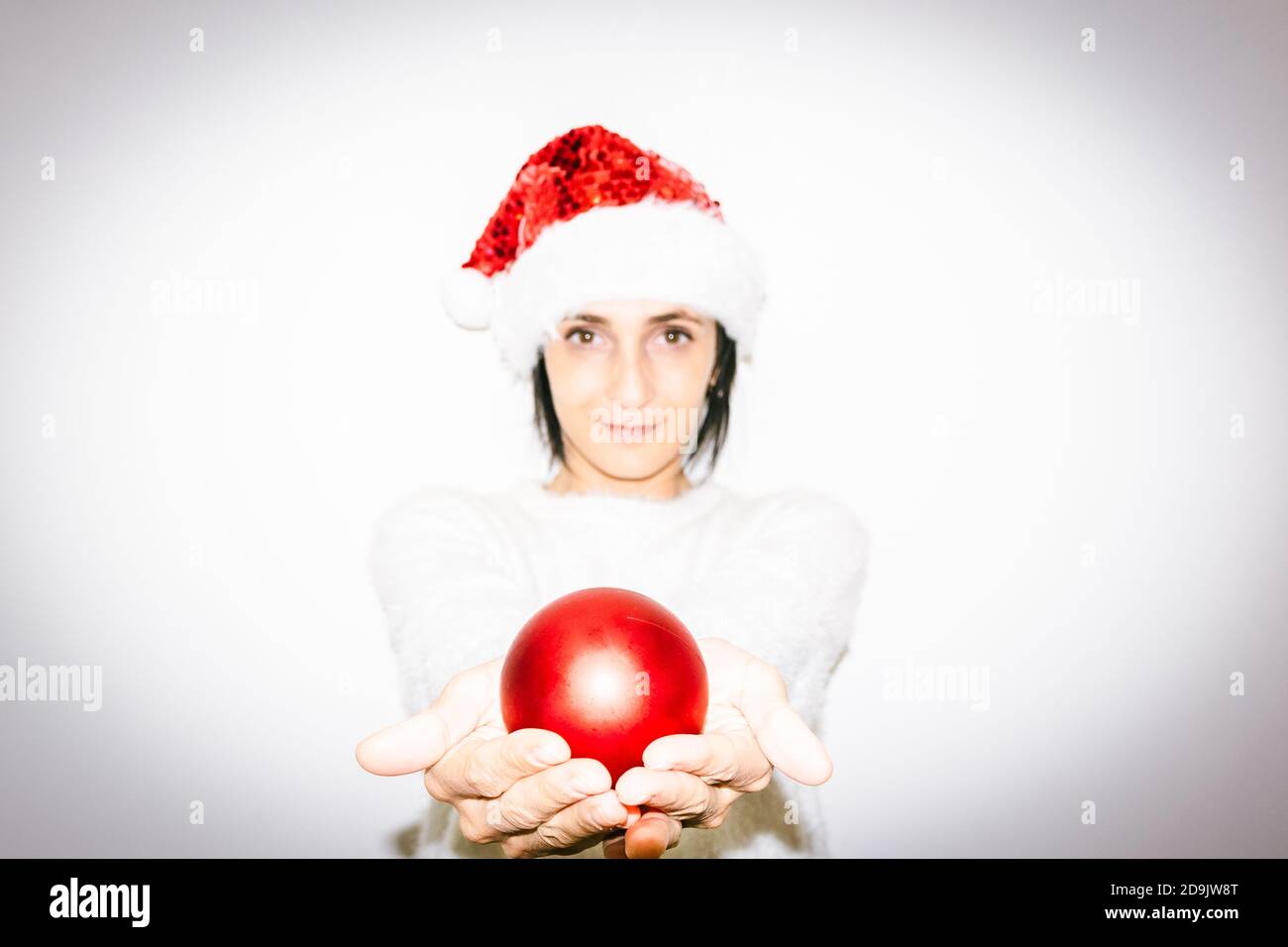Woman in Christmas outfit holds in two hands red xmas decoration shiny ball gift. Happiness and sharing of love  and hope on celebrations Stock Photo