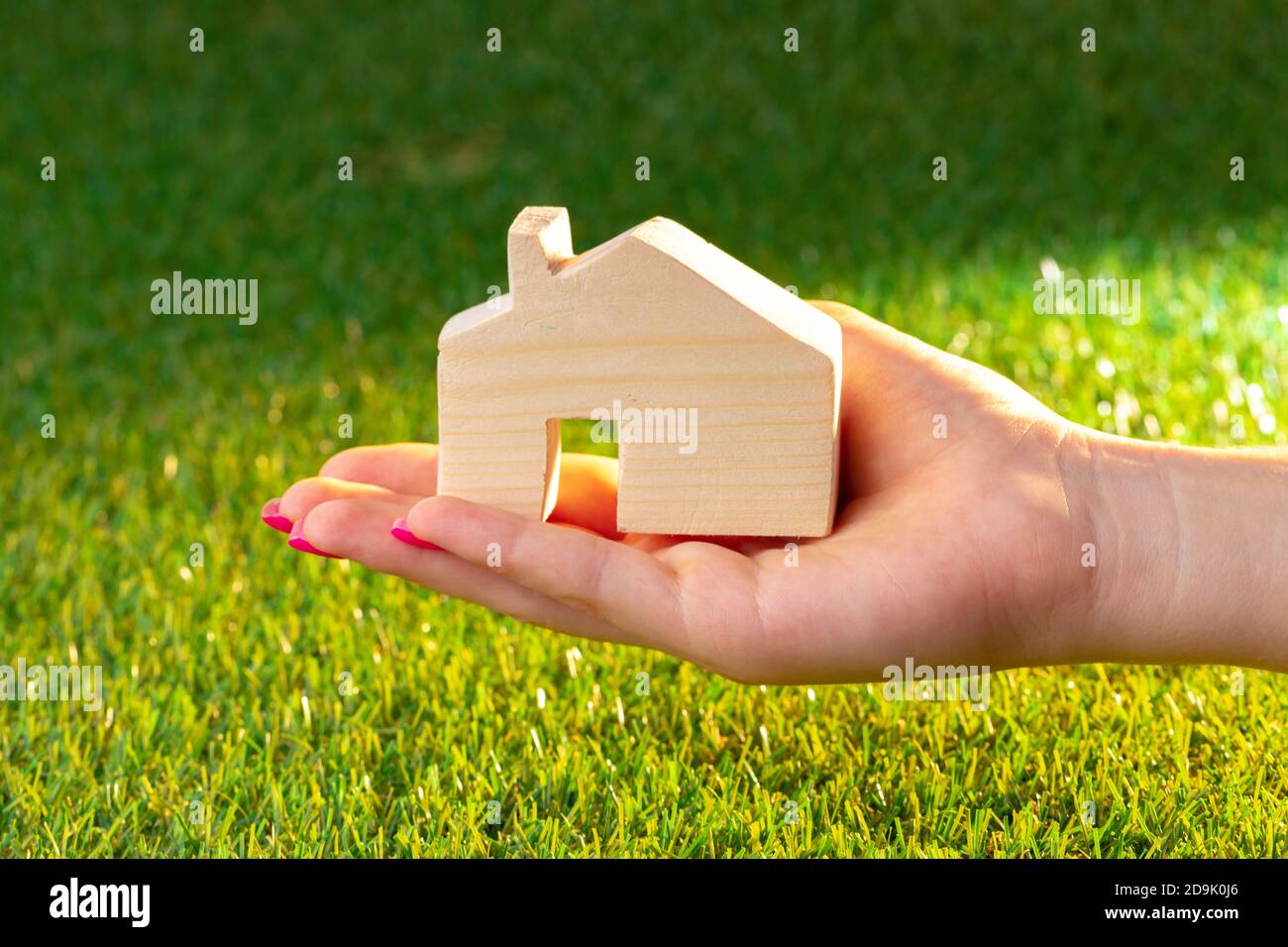 Female hand holding wooden house model above the grass Stock Photo - Alamy