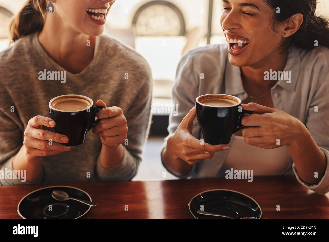 Two females sitting at a coffee table talking and laughing. Happy woman friends in a cafe having coffee. Stock Photo