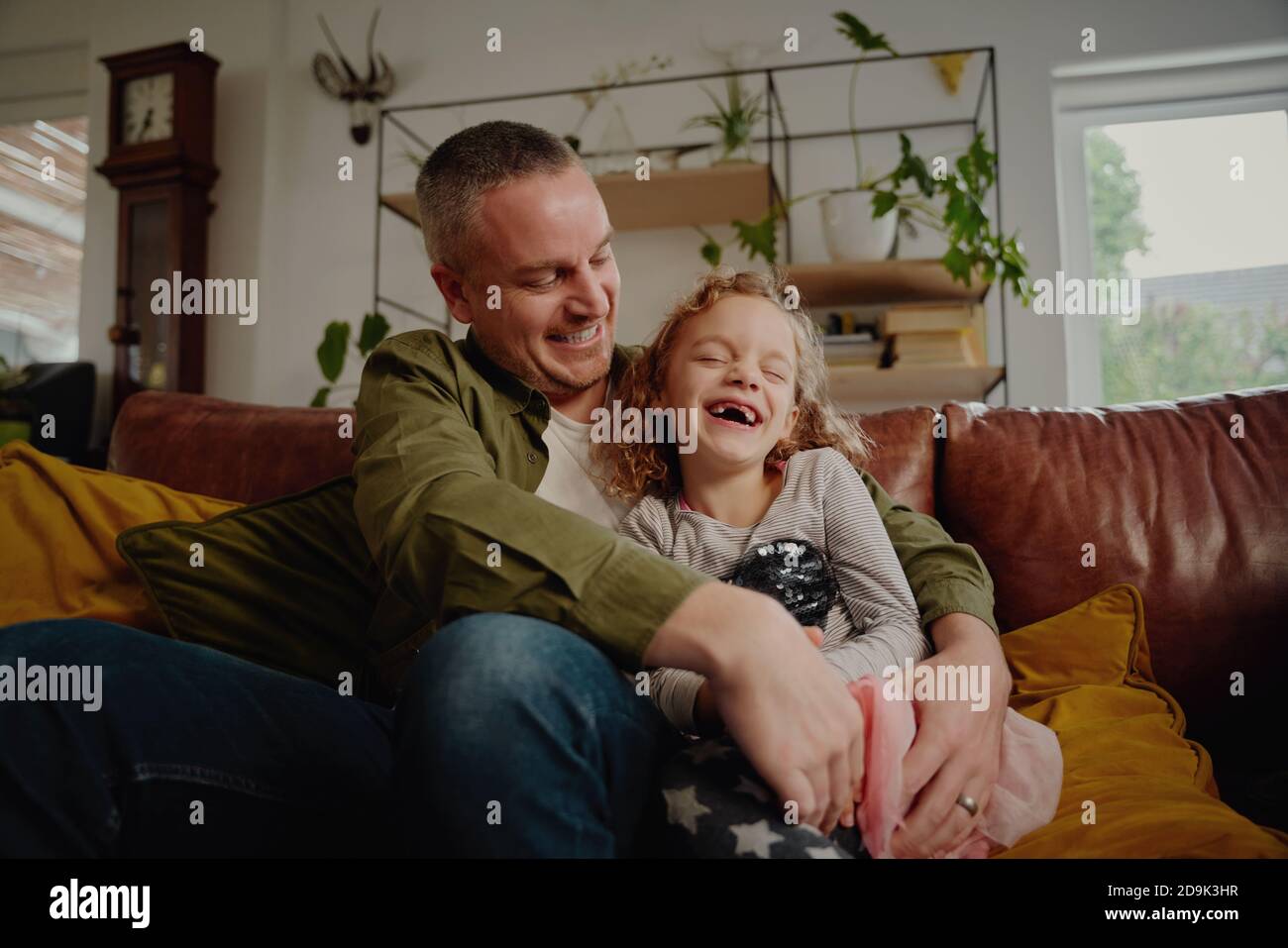 Cheerful father and daughter playing and laughing sitting on couch at home Stock Photo