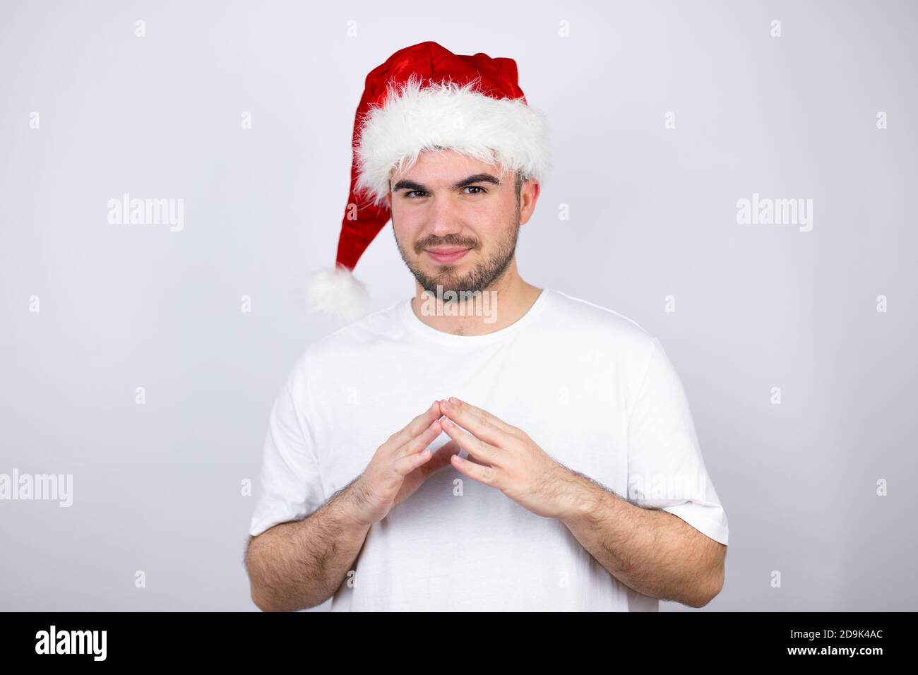 Young handsome man wearing a Santa hat over white background with Hands ...