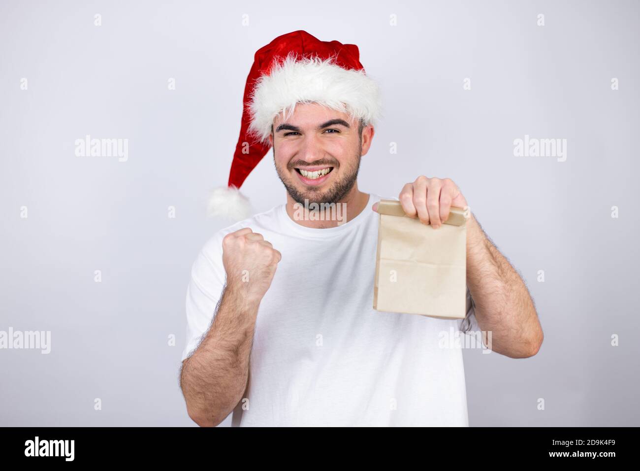 Young handsome man wearing a Santa hat over white background holding a ...