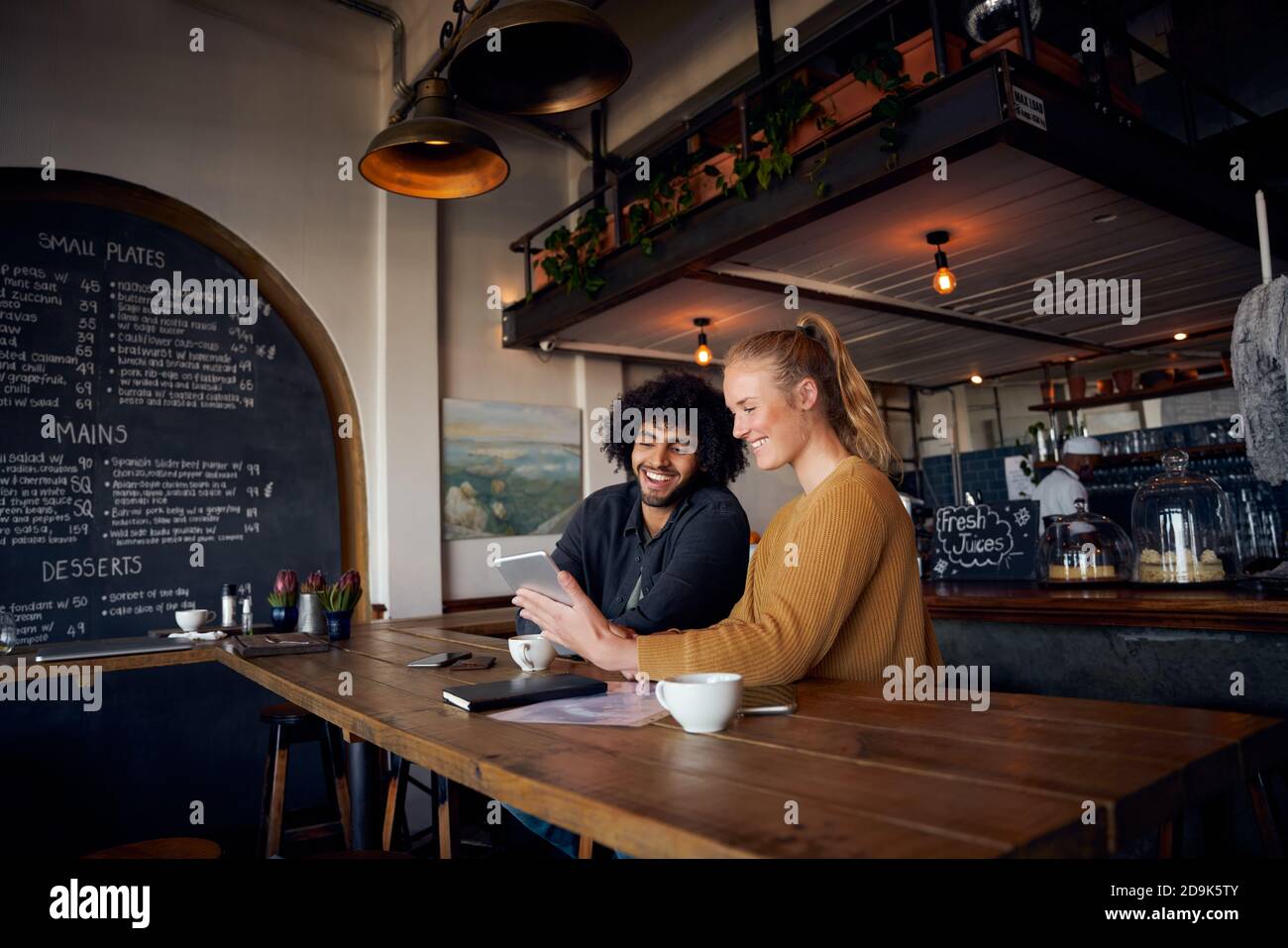 Happy young couple sitting and relaxing in cafe using digital tablet to watch videos Stock Photo