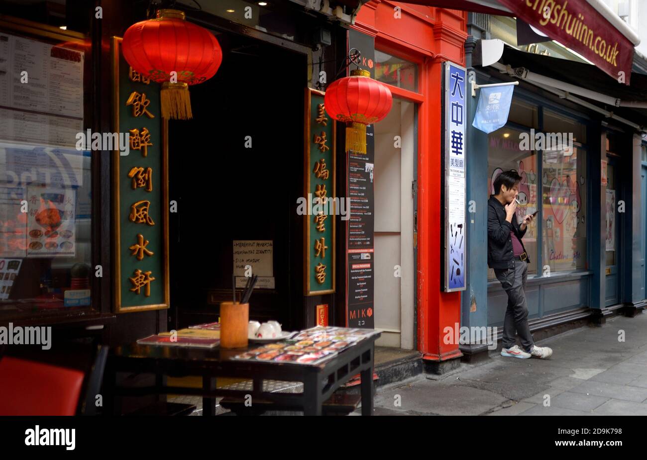 London, England, UK. Chinatown: Gerrard Street - young Chinese man looking at his mobile phone and smoking a cigarette Stock Photo