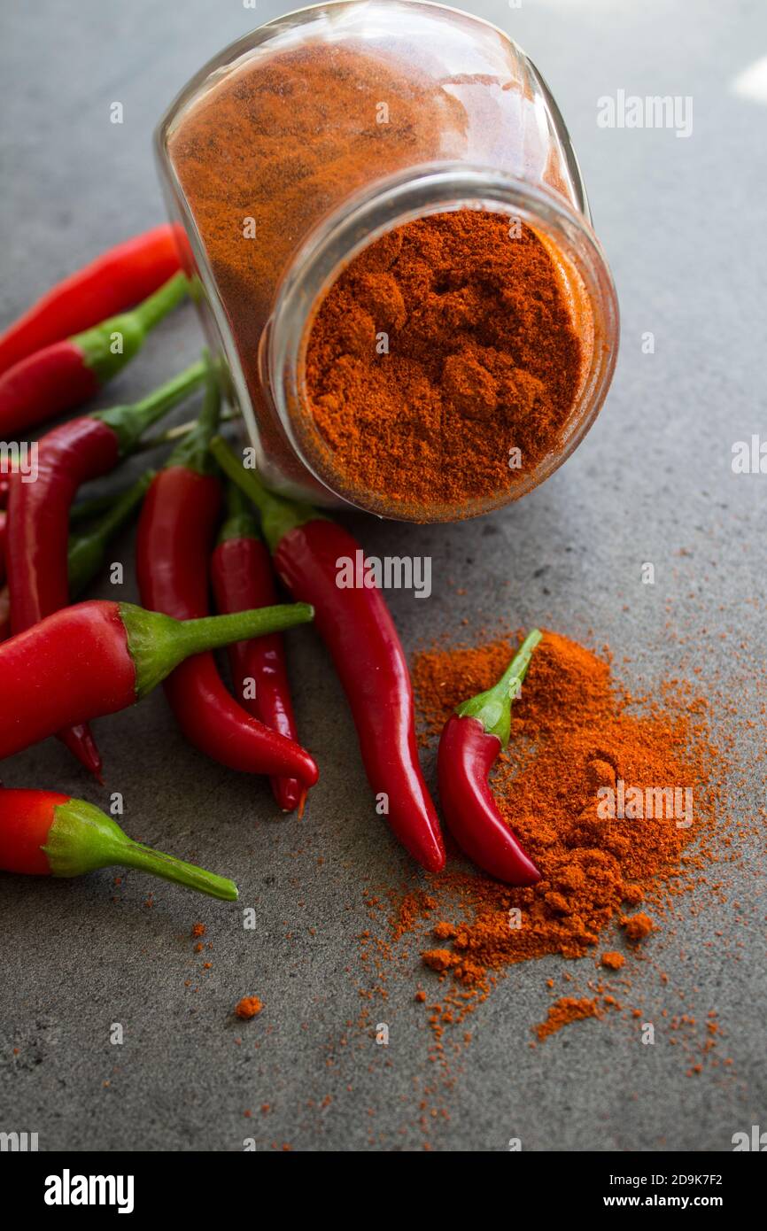 Red chili peppers and paprika powder in glass spice jar on stone table